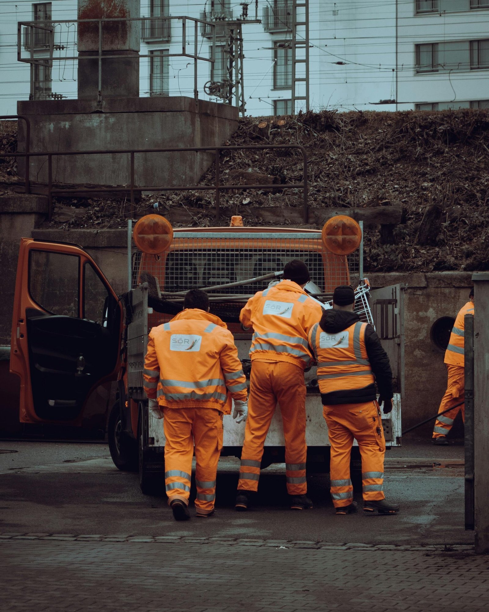 Group of construction workers in orange safety uniforms at a job site in a city.